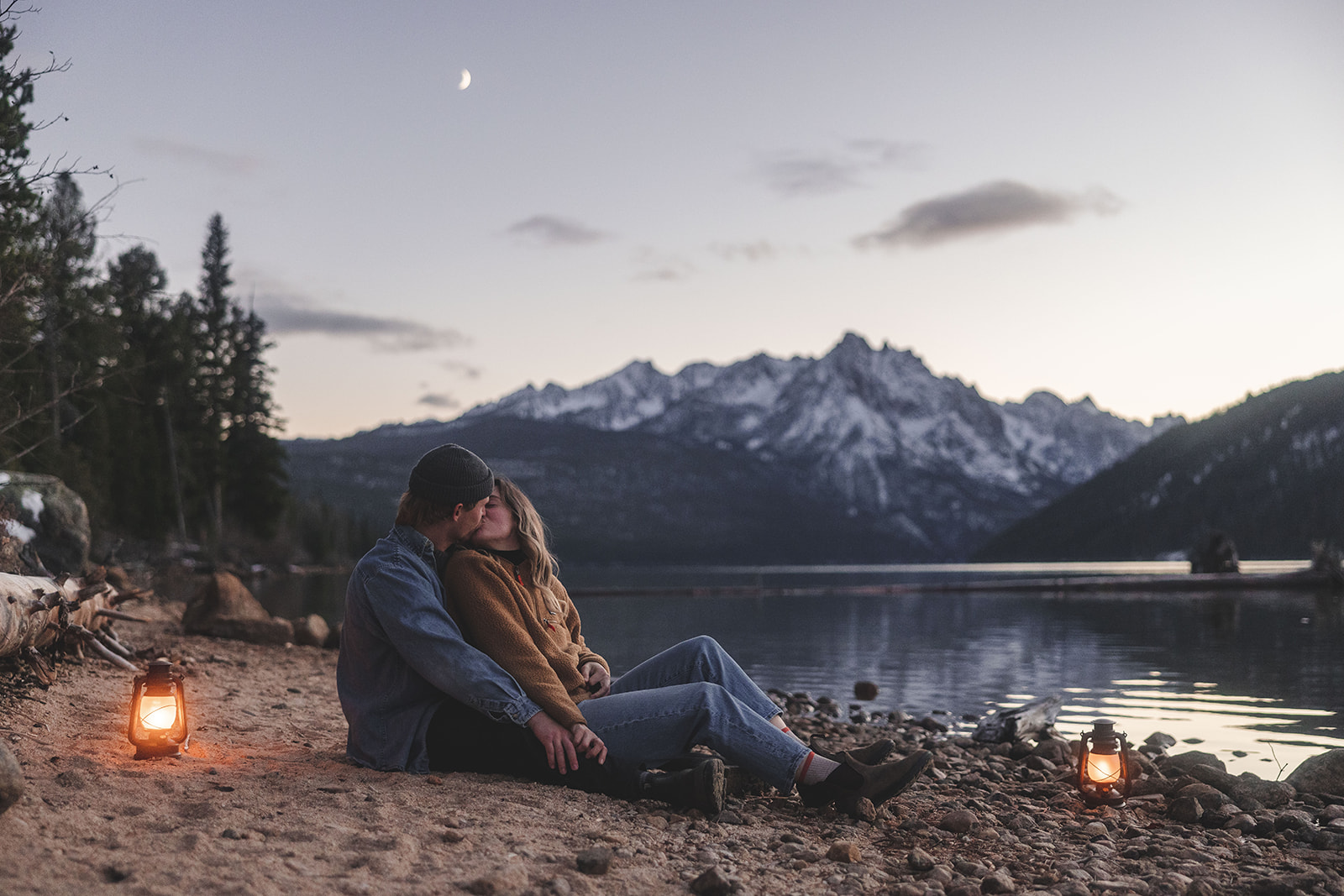 Husband and wife sit on log for an engagement near the Sawtooth Mountains